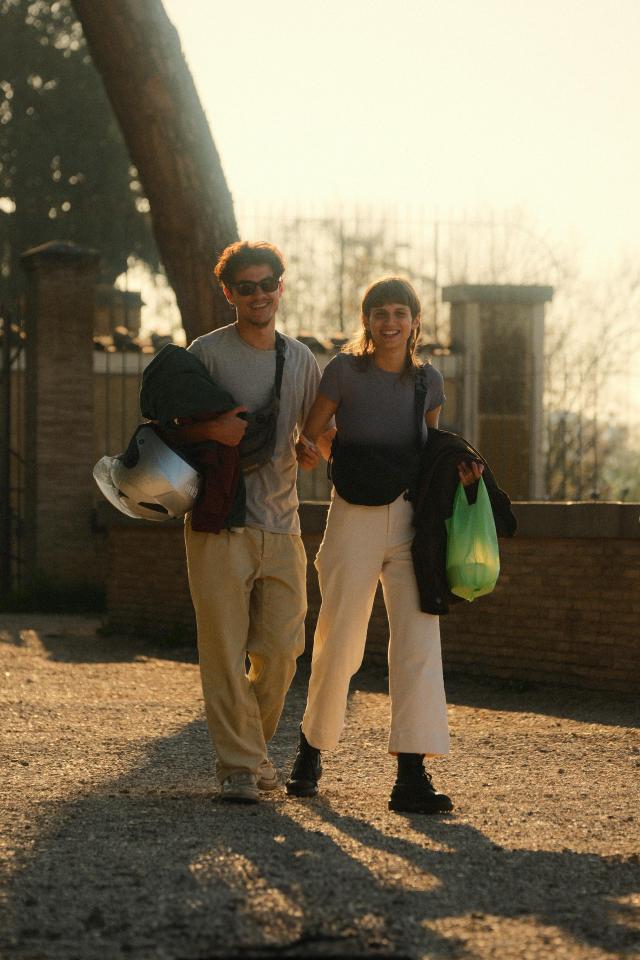 A smiling young couple walks in sunlight, enjoying an outdoor stroll together.