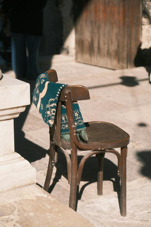 Sunlit vintage wooden chair draped with an artistic blue patterned blanket outdoors.